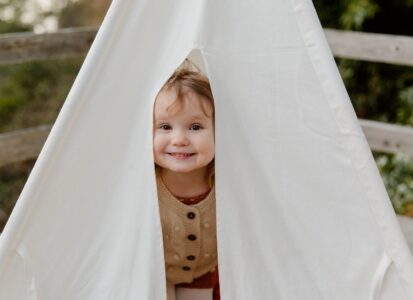 happy little child smiling while peeking from tent