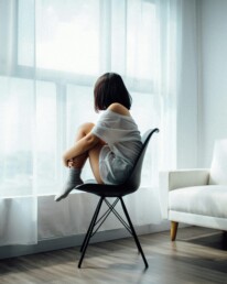 woman sitting on black chair in front of glass-panel window with white curtains